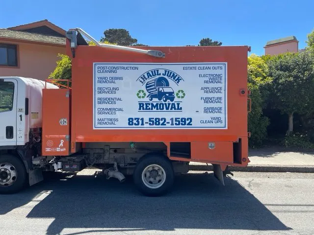 Junk removal Company in Monterey A white and orange Haul Junk removal truck parked on a street with residential buildings in the background.